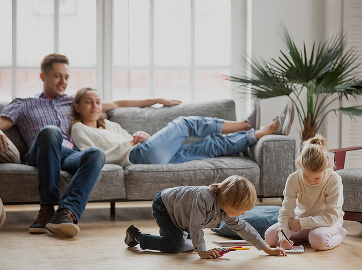 Family enjoying quality time at home, with parents relaxing on a sofa and children engaged in creative play on the floor, emphasizing comfort and family bonding in a cozy living space.