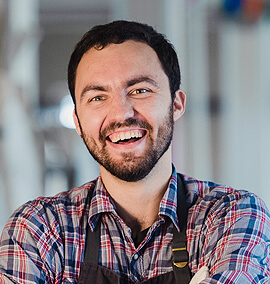 Smiling male HVAC technician in plaid shirt, representing the dedicated team at PROTECH HVAC, showcasing expertise in heating and air conditioning services.