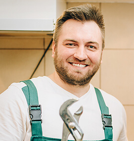 Smiling HVAC technician in green overalls holding a wrench, representing the dedicated team at PROTECH HVAC, LLC.