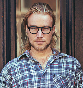 Young man with long hair and glasses wearing a plaid shirt, representing the team at PROTECH HVAC, showcasing expertise in HVAC services.