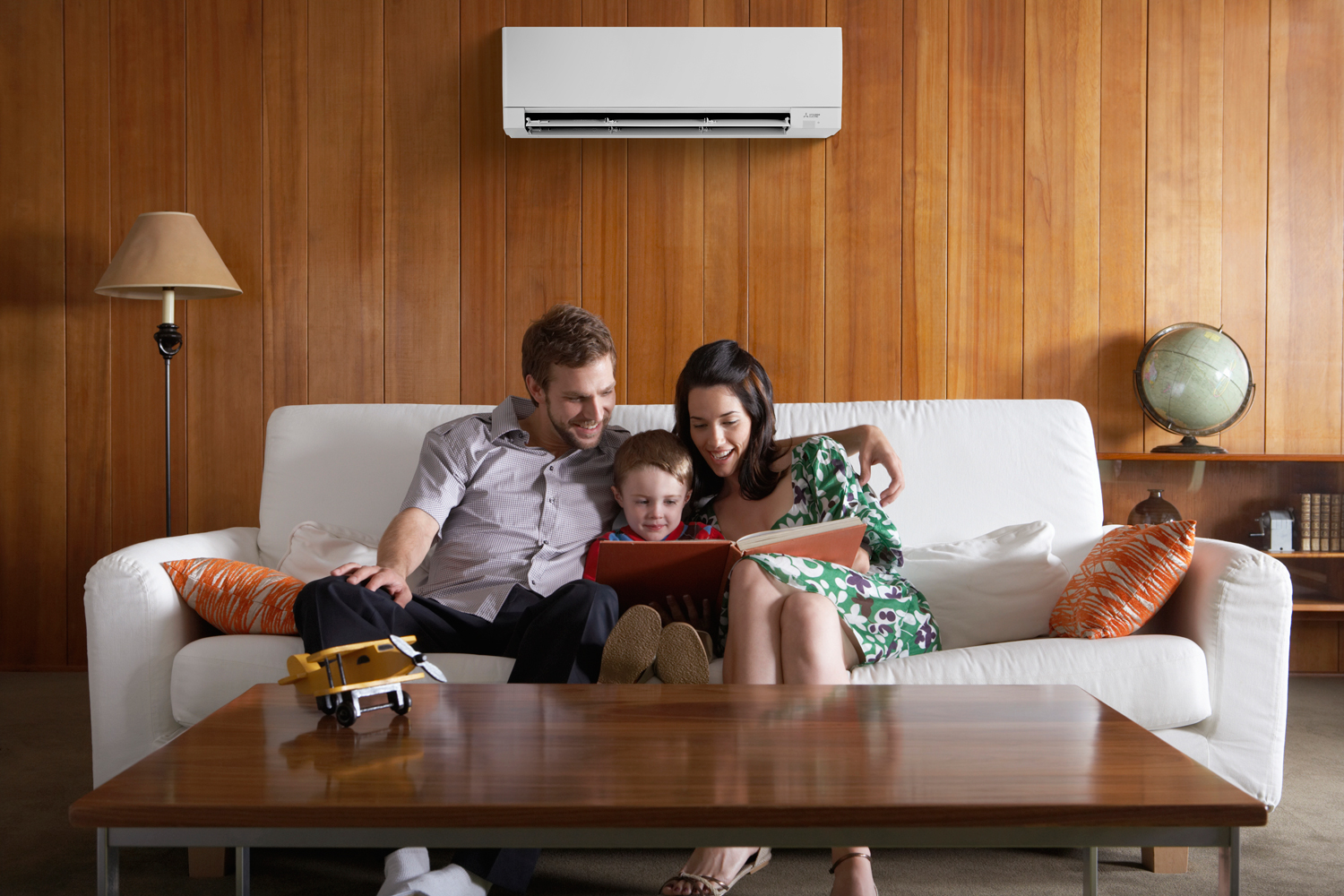 Family enjoying time together on a couch, reading a book, with a modern ductless mini-split HVAC system installed above, showcasing comfort and energy-efficient home climate solutions.